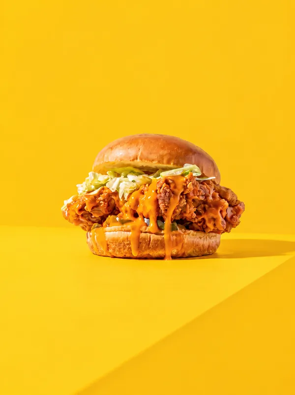 Burger de frango crocante com molho e salada no fundo amarelo